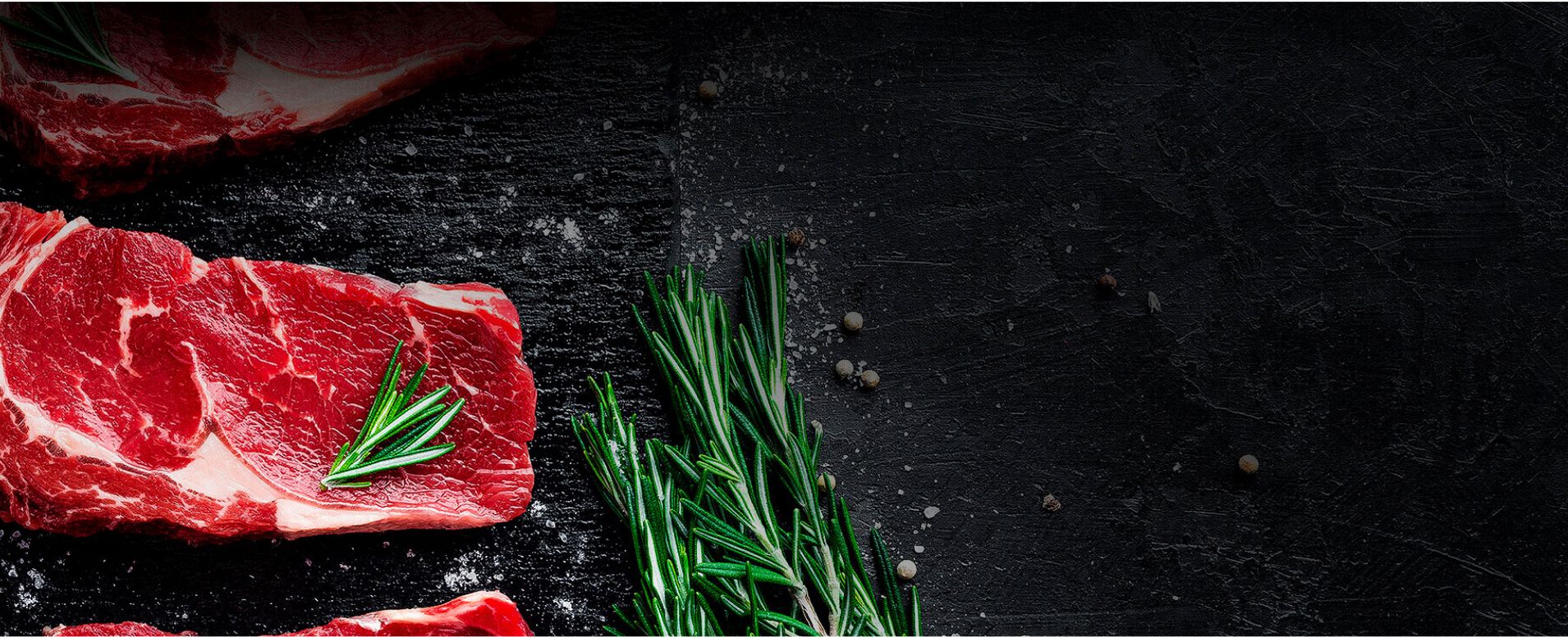 Rohes Fleisch, angerichtet auf einer schwarzen Platte mit Kräutern.